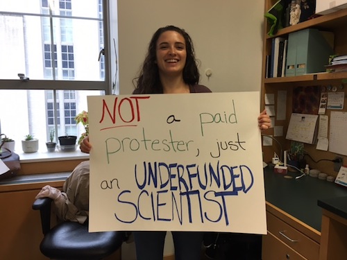 Woman holding a protest sign in her office.